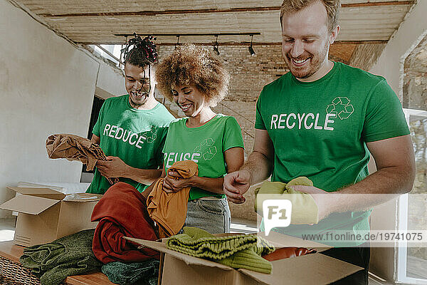 Smiling activists putting secondhand clothes in cardboard boxes at apartment