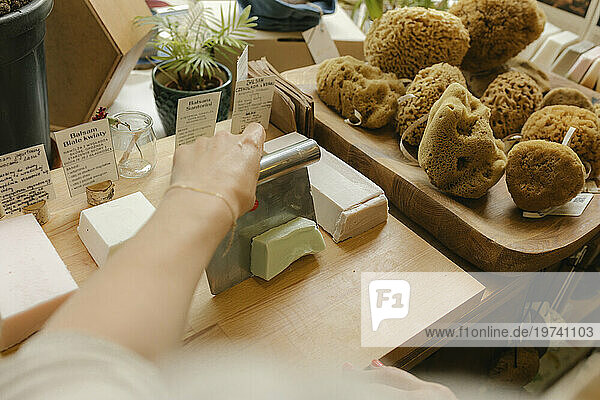 Hand of woman owner cutting bar of soap on table in store