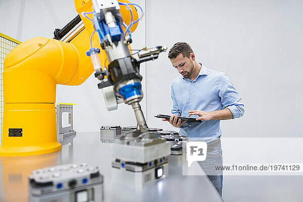 Engineer using tablet PC near robotic arm in factory