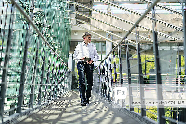 Businessman walking in corridor of modern office building using digital tablet