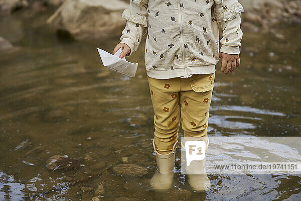 Girl holding paper boat and standing in water puddle
