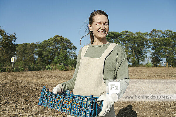 Happy farmer holding crate of potatoes harvested from field
