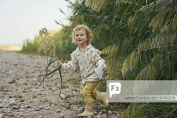 Happy girl holding twig and running near plants