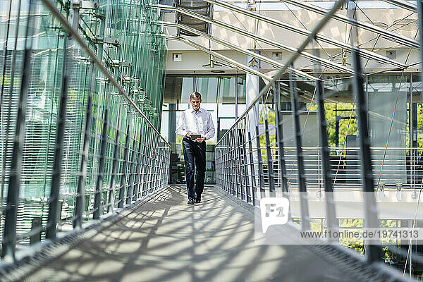 Businessman walking in corridor of modern office building using digital tablet
