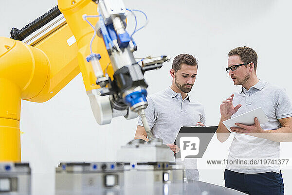 Engineers with tablet PC and file folder having discussion near robotic arm in factory