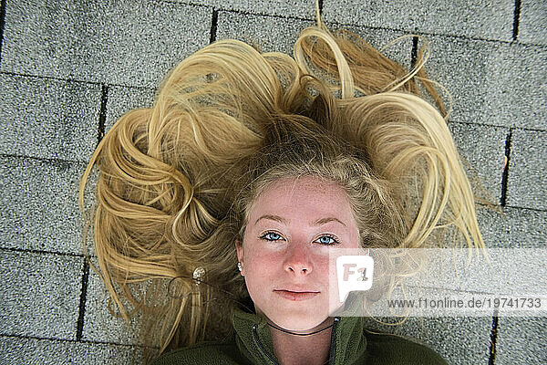 Teenage girl with long blond hair lays on shingled roof; Elkhorn  Nebraska  United States of America