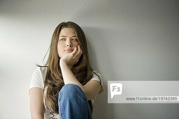 Portrait of a young adult woman sitting and leaning against a white wall; Fairbanks  Alaska  United States of America