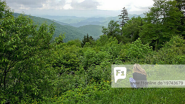 View taken from behind of of a woman crouching down to take in the view of the Blue Ridge Mountains along the Blue Ridge Parkway; North Carolina  United States of America