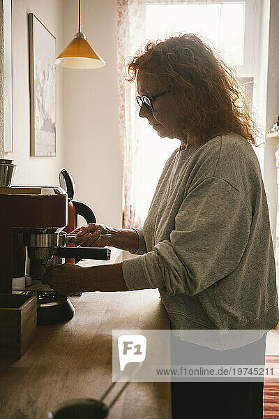 Side view of senior woman making coffee in kitchen at home