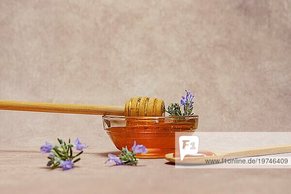 Natürlicher Honig in einer Glasschale mit einem Holzlöffel und frischen Rosmarinzweigen in Blüte