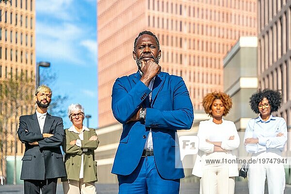 Frontalporträt eines reifen afrikanischen Geschäftsmannes im Anzug  der ernsthaft neben seinen Kollegen steht
