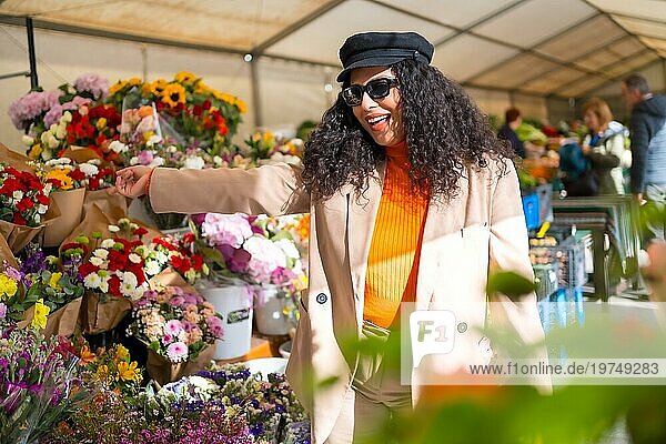 Glückliche lateinische Frau wählt Blumen in einem Blumenladen im Freien auf einem Straßenmarkt an einem sonnigen Wintertag aus