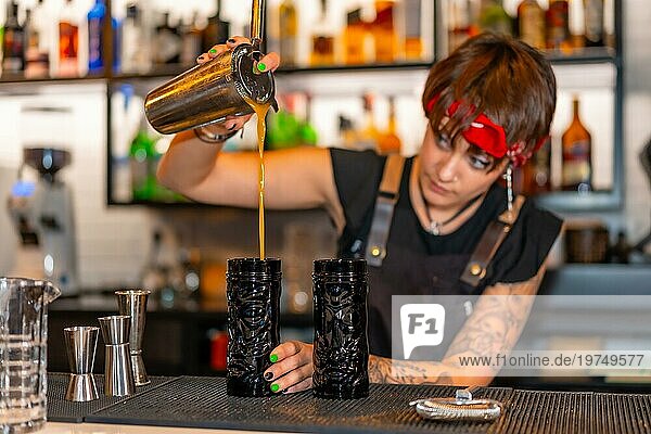 Alternativer junger Barkeeper  der einen Cocktail in ein kreatives Glas an der Theke einer Bar einschenkt