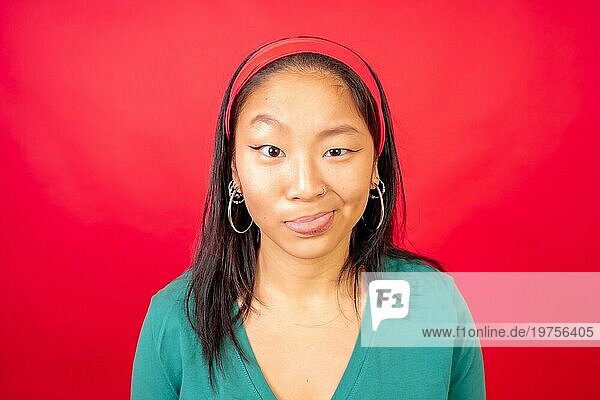 Studiofoto mit rotem Hintergrund von einer chinesischen Frau  die lustige Grimassen in die Kamera macht