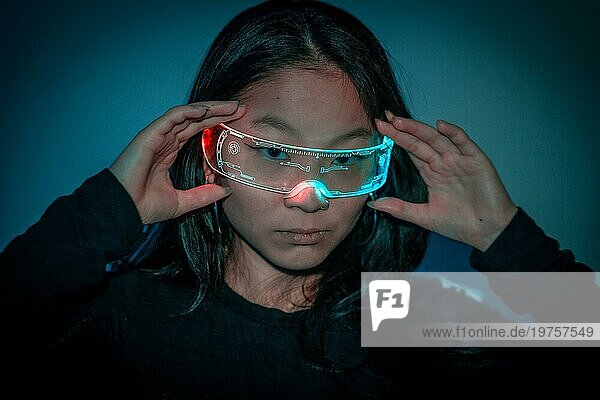 Studiofoto mit blauem Hintergrund mit Neonlicht von einer chinesischen Frau mit kybernetischer Brille  die in die Kamera schaut