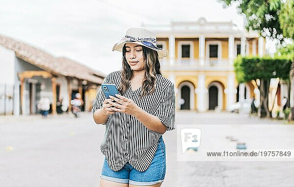 Schöne junge Touristin mit Hut und Telefon auf der Straße. Latin Tourist Mädchen Texting mit Telefon auf der Straße