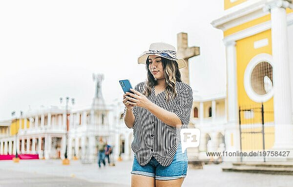 Weibliche Touristin beim Telefonieren auf dem Platz von Granada. Lächelnder junger Tourist mit Hut benutzt Handy auf der Straße