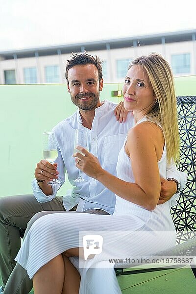 Vertikales Porträt von Liebenden  die ihre Liebe mit Champagner feiern  auf einem Stuhl auf der Terrasse eines Hotels sitzend