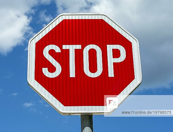 Rotes achteckiges Stoppschild an einem Metallmast mit bewölktem Himmel im Hintergrund. Straße Stop Symbol