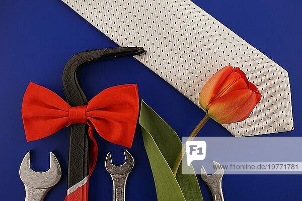Brechstange mit roter Schleife  Schraubenschlüssel  Krawatte und Tulpe auf blauem Hintergrund und freiem Platz für Ihren Gruß