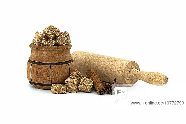 Braune Rohrzuckerwürfel in hölzerner Zuckerdose neben Zimtstangen  Sternanis und Nudelholz. Süßwaren Konzept vor weißem Hintergrund