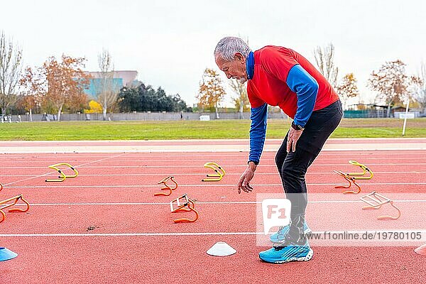 Sportlicher älterer Mann beim Aufstellen von Kegeln und Startblöcken auf einer Leichtathletikbahn für das Training im Freien im Winter