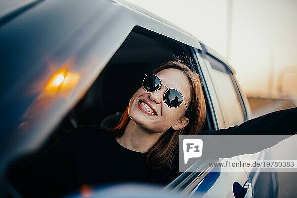 Glückliche Autofahrerin mit Sonnenbrille fährt ein Auto und lächelt bei Sonnenuntergang. Glückliche Reise Konzept