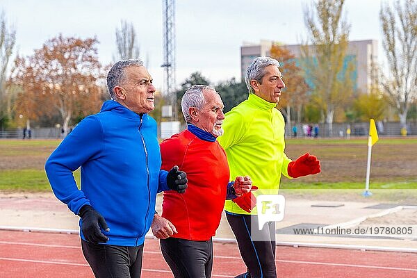 Ältere  sportliche Männer in bunter Sportkleidung  die gemeinsam auf einem Leichtathletikplatz laufen