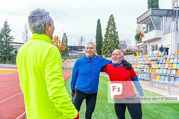 Drei ältere Männer im Ruhestand wärmen sich gemeinsam auf einem Leichtathletikplatz auf