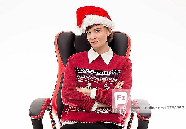 Bild einer schönen Frau in einem Weihnachtspulli  die auf einem Bürostuhl vor einem weißen Hintergrund posiert. Feiertags Konzept. Firmenveranstaltungen. Gemischte Medien