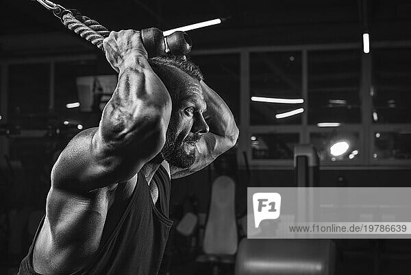 Bild eines kraftvollen Athleten  der in einem Crossover im Fitnessstudio trainiert. Trizeps pumpt. Fitness und Bodybuilding Konzept. Gemischte Medien