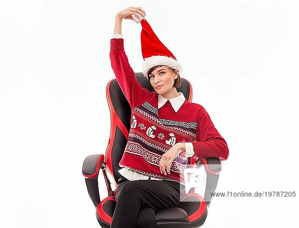 Bild einer schönen Frau in einem Weihnachtspulli  die auf einem Bürostuhl vor einem weißen Hintergrund posiert. Feiertags Konzept. Firmenveranstaltungen. Gemischte Medien