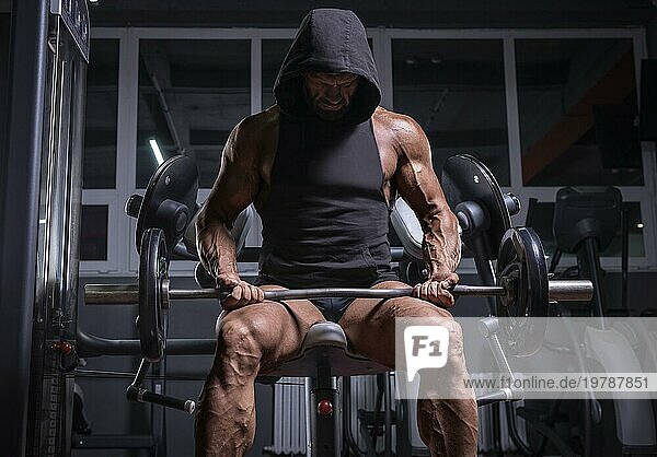 Bild eines kräftigen Athleten in einem Hoodie  der auf einer Bank in einem Fitnessstudio sitzt. Fitness und Bodybuilding Konzept