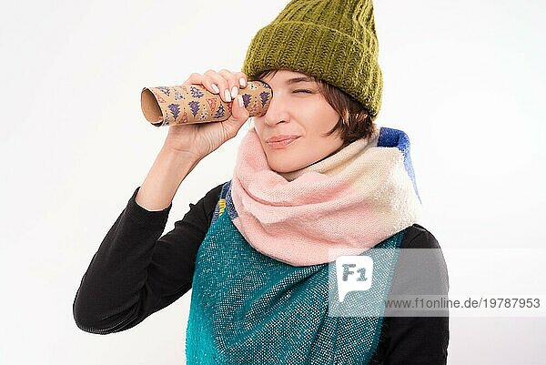 Porträt einer lächelnden Frau mit Wintermütze und Schal  die durch festliches Geschenkpapier blickt. Feiertags Konzept. Gemischte Medien