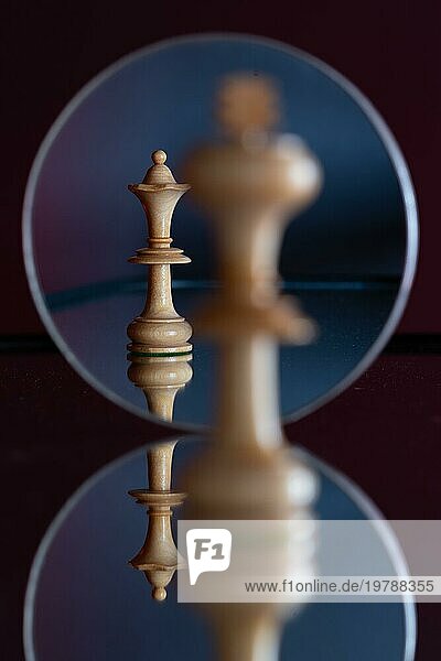 Eine Dame-Schachfigur ist in einem Spiegel zu sehen  davor steht ein König auf sich spiegelndem Untergrund  Schachspiel  Symbolbild für Macht  Beziehung  Konflikt