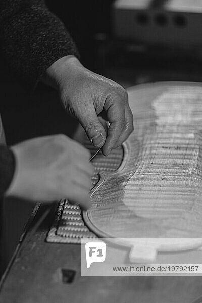 Unerkannte Hände eines Geigenbauers in seiner Werkstatt probieren  schieben und kleben Filetstreifen in einen geschnitzten Intarsienkanal für einen neuen rohen Boden und eine neue Vorderplatte einer klassischen handgefertigten Geige in Cremona  Italien  Europa