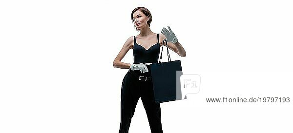 Ein elegantes großes Mädchen mit weißen Handschuhen zeigt ein schwarzes Luxuspaket. Das Konzept des sicheren Einkaufens während einer Pandemie. Gemischte Medien
