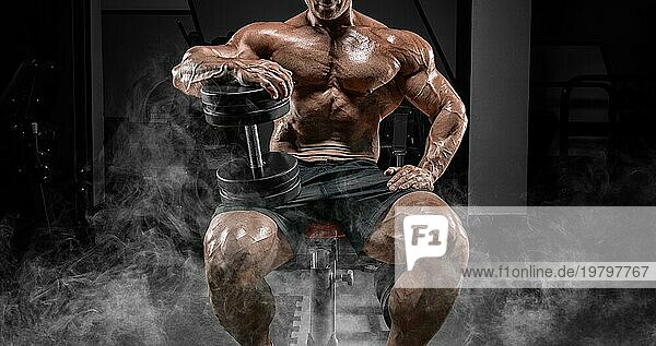 Muskulöser Mann sitzt auf einer Bank im Rauch mit Hanteln. Bodybuilding und Kraftdreikampf Konzept.