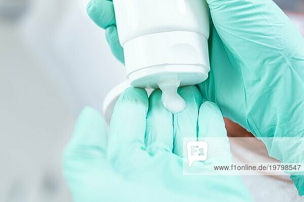 Bild von Händen in medizinischen Handschuhen  die Creme aus einer weißen Tube auspressen. Konzept zur Hautpflege.