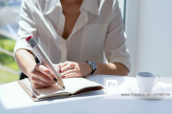 Das Mädchen schreibt in einem Notizbuch mit einem großen Bleistift. Konzept von Vorstellungsgespräch  Geschäft  Erfolg. Gemischte Medien