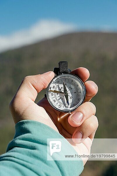 Nahaufnahme Die Hand eines Mannes hält einen Taschenkompass vor dem Hintergrund von Bergen und Wäldern. Das Konzept der Outdoor Navigation