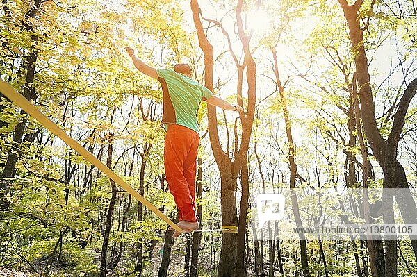 Rückansicht bärtiger Mann im Alter geht an einem sonnigen Nachmittag im Herbstwald an einer Slackline entlang. Das Konzept der Freizeit und Erholung von aktiven Menschen mittleren Alters
