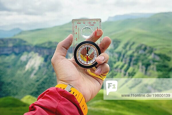 Männliche Hand hält einen magnetischen Kompass auf dem Hintergrund von Hügeln und dem Himmel mit Wolken. Das Konzept des Reisens und der Suche nach dem eigenen Lebensweg