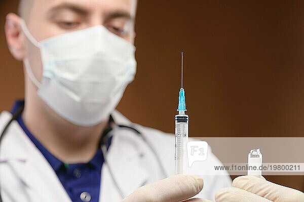 Junger kaukasischer Arzt im weißen Kittel  der eine Spritze mit einem Impfstoff hält. Fokus auf die Spritze