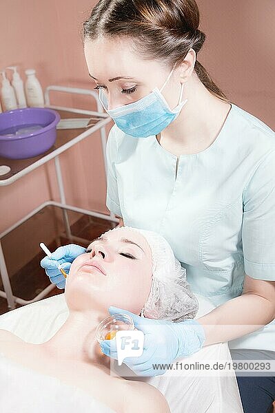 Im Büro einer Kosmetikerin legt eine Kosmetikerin einer attraktiven Kundin eine verjüngende Maske auf das Gesicht. Professionelle kosmetische Dienstleistungen