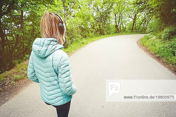 Porträt eines attraktiven  sportlichen  blonden Mädchens  das auf einem Waldweg von hinten nach unten läuft und Bluetooth Kopfhörer mit Musik oder Naturgeräuschen trägt