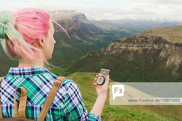 Ein Hipster Mädchen reiste mit einem Blogger in einem karierten Hemd und mit bunten Haaren mit einem Kompass im Hintergrund in den Hintergrund der kaukasischen Landschaft mit einem Plateau