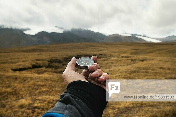 Die Hand eines Reisenden hält einen Magnetkompass vor dem Hintergrund einer Berglandschaft und niedriger Wolken an einem sonnigen Tag in den Bergen. Navigieren und die richtige Richtung finden