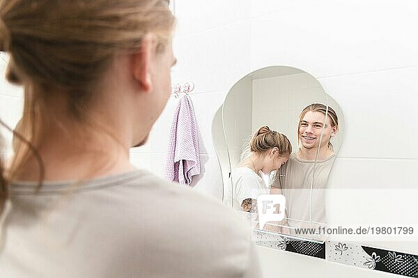 Junges heterosexuelles Paar lacht vor dem Badezimmerspiegel am Morgen