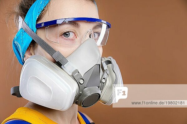 Porträt einer jungen kaukasischen Frau in Schutzausrüstung für die Seh und Atmungsorgane. Blick in die Kamera. Ein Mädchen mit Atemschutzmaske und Schutzbrille in einem Arbeitsanzug. Studioaufnahme